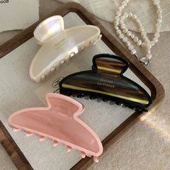 Three claw clips in pink, cream, and brown tortoiseshell patterns arranged on a wooden tray.