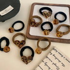 Assortment of leopard print hair ties with round and heart charms, displayed on a surface with fabric.