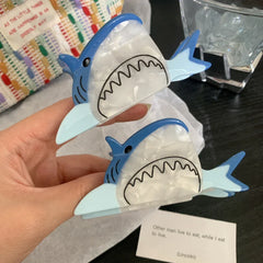 A hand holding two blue and white shark hair clips