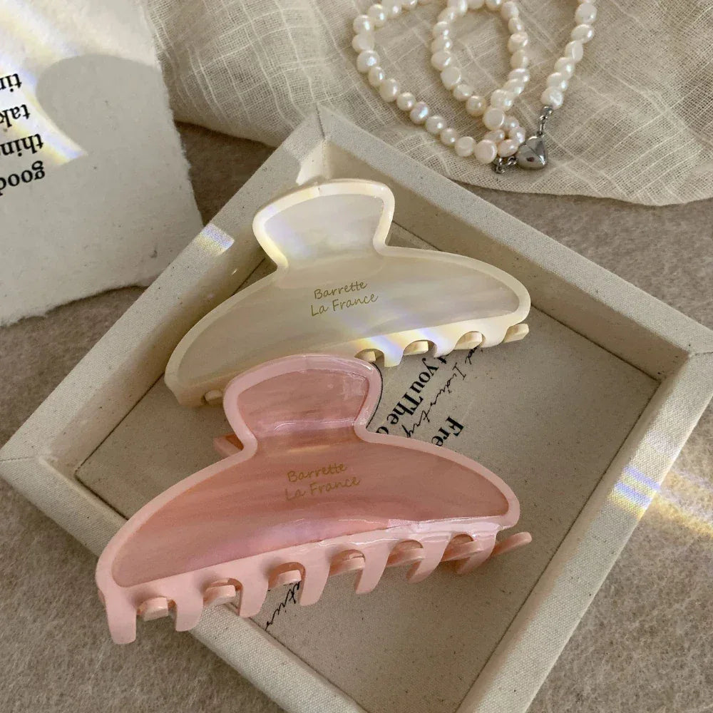 Two claw clips in cream and pink arranged on a textured surface within a tray.