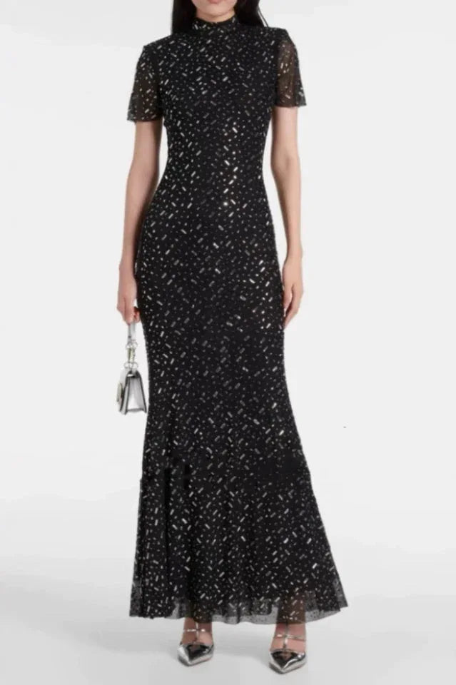 Full-length view of a black sequined gown with a high neckline and short sleeves, with a silver clutch.
