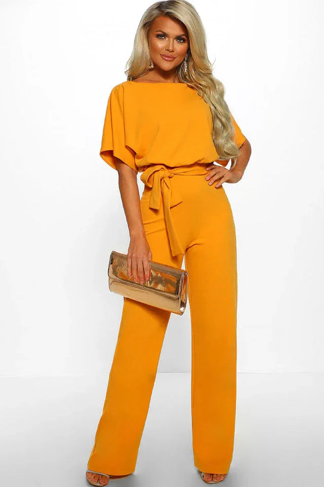 Woman wearing an orange wide leg jumpsuit with a tie waist and boat neck