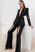 Woman wearing a black suit with cut-out details and decorative trim, posing on a white cube.
