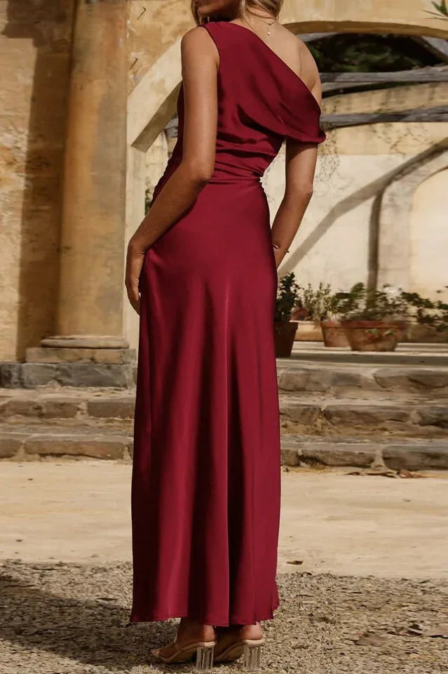 Back view of a woman in a burgundy one-shoulder satin maxi dress.