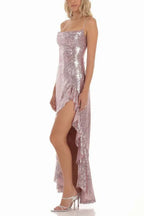 woman wearing a rose gold sequined gown with a high slit and ruffle trim, side view