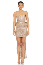 Woman wearing a strapless gold sequined mini dress with a large bow and train