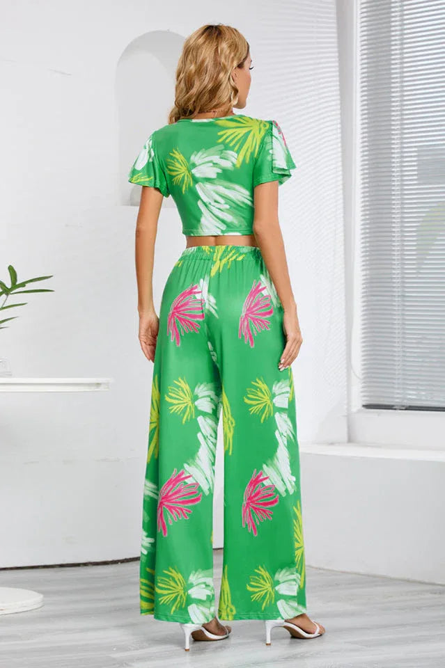 Woman wearing a green floral print two-piece set with a cropped V-neck top and wide-leg pants, back view. Secondary image