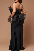 Rear view of a plus-size woman wearing a black strapless formal gown with a ruffled peplum bodice and mermaid skirt.