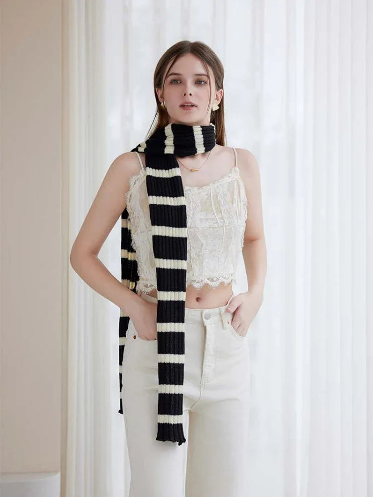Woman wearing a black and white striped scarf with a white lace top and cream pants Main image