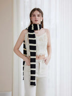 Woman wearing a black and white striped scarf with a white lace top and cream pants