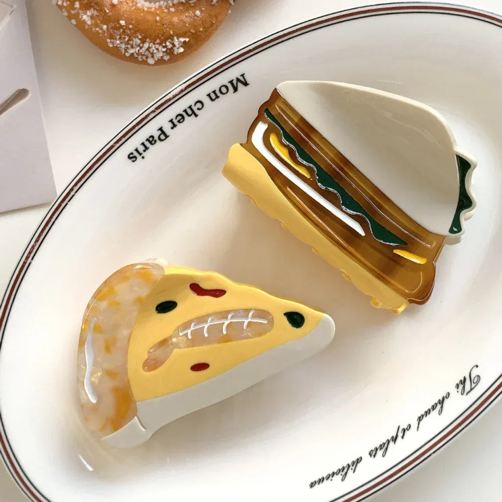 acrylic slice of pizza hair clip and a sandwich hair clip on a white plate with text that says 'Mon cher Paris'