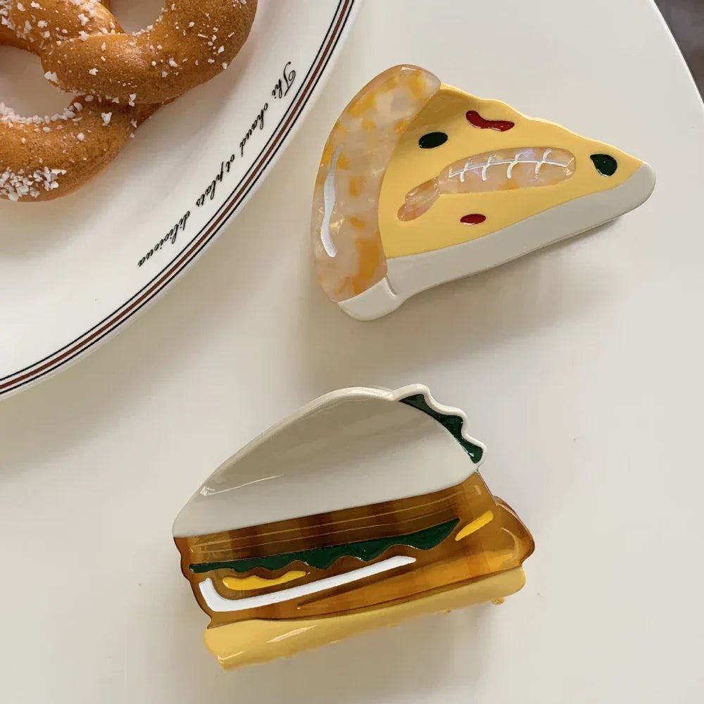 overhead view of acrylic slice of pizza hair clip and sandwich hair clip on a white surface next to pretzels