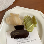 Three acetate claw hair clips in beige, green, and brown arranged on a white plate.