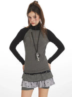 Close-up of model wearing a gray and black long-sleeve turtleneck top with a layered skirt and necklace.