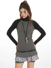 Close-up of model wearing a gray and black long-sleeve turtleneck top with a layered skirt and necklace.