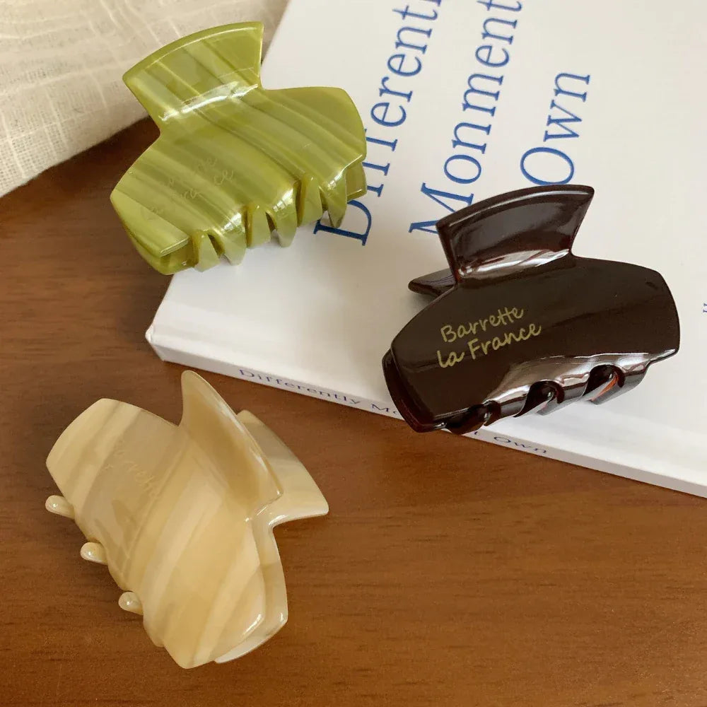 Three acetate claw hair clips in beige, green, and brown resting on a book.