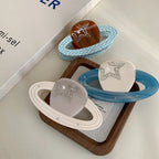 Three planet-shaped hair clips in different colors (brown, white, grey) with rings and star embellishments, arranged on a tray.