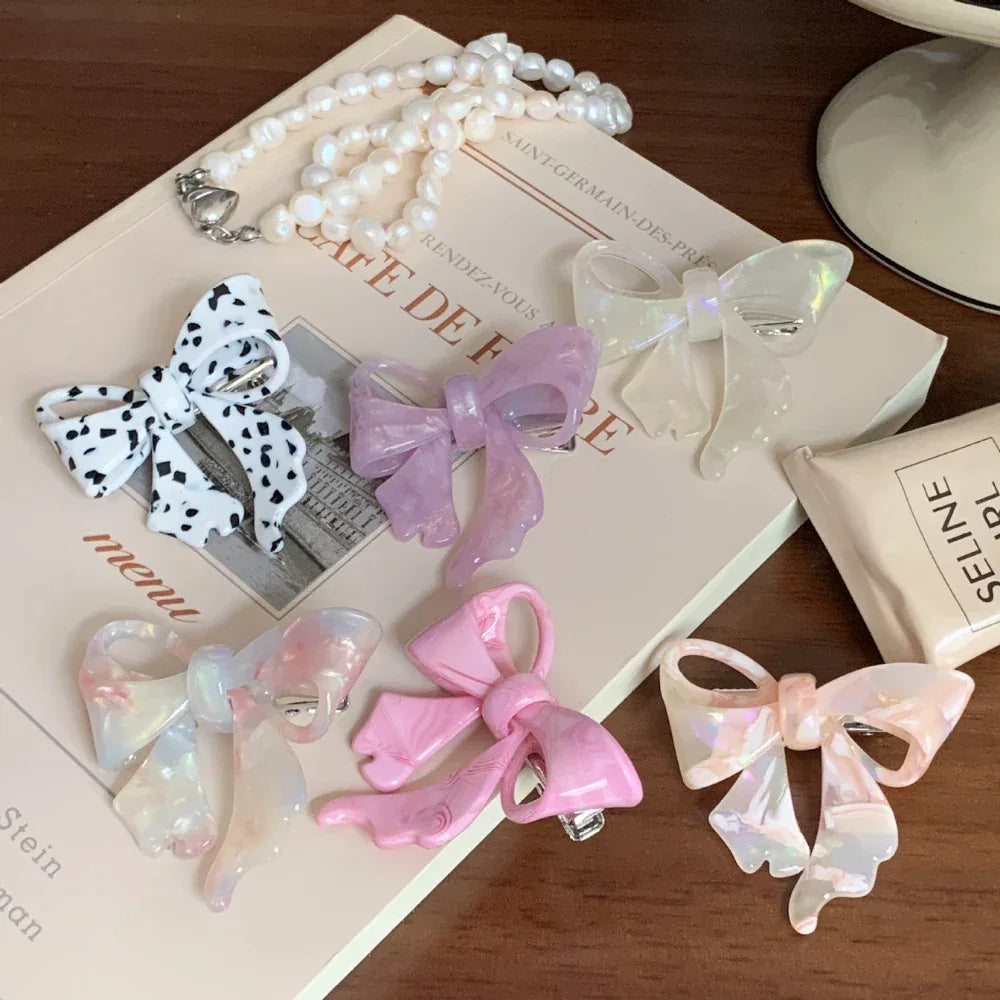 A variety of bow hair clips, including a dalmatian print and pastel colors, displayed on a book and tray.
