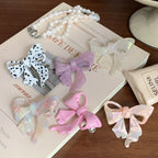 A variety of bow hair clips, including a dalmatian print and pastel colors, displayed on a book and tray.
