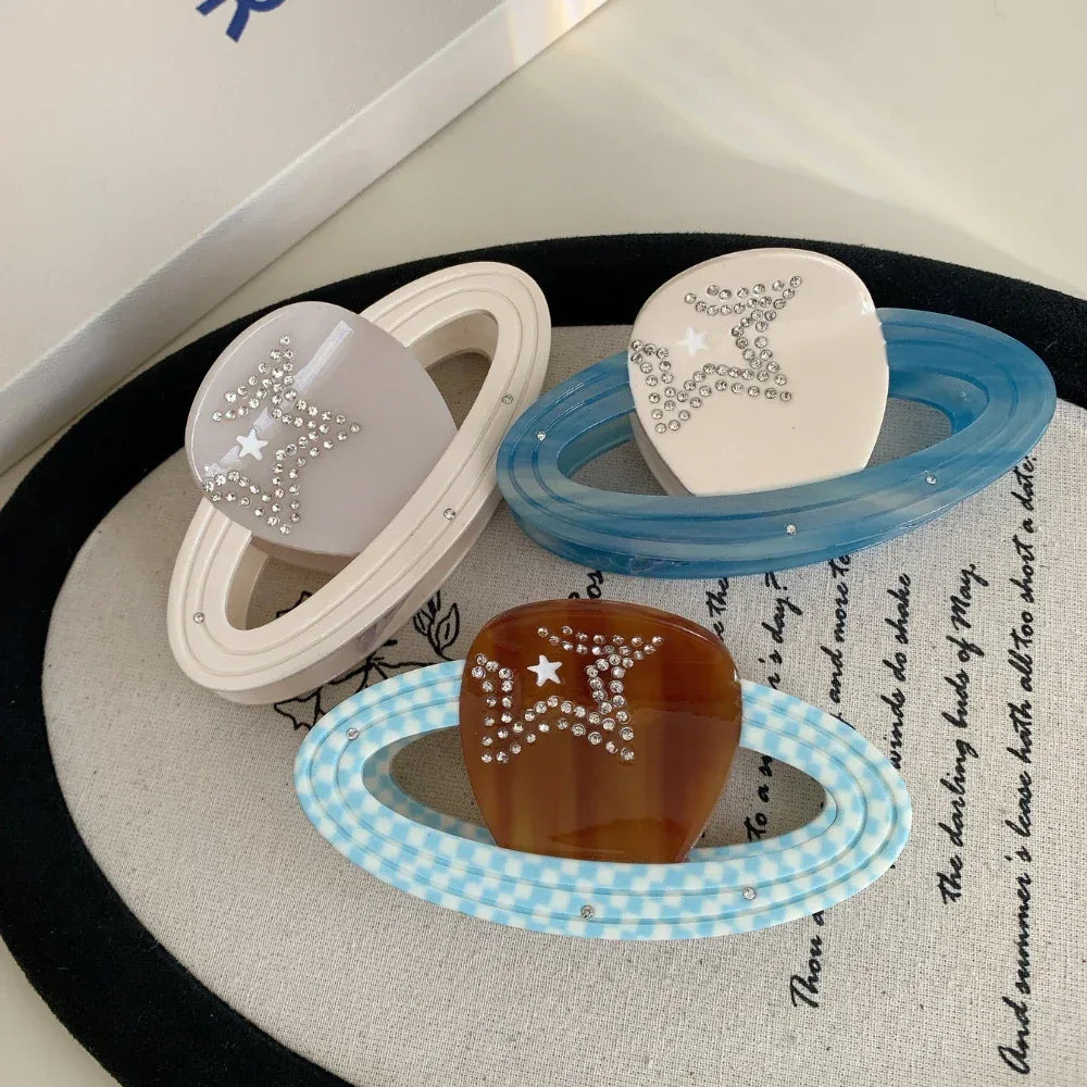 Three planet-shaped hair clips with rings and star embellishments, displayed on a circular mat.