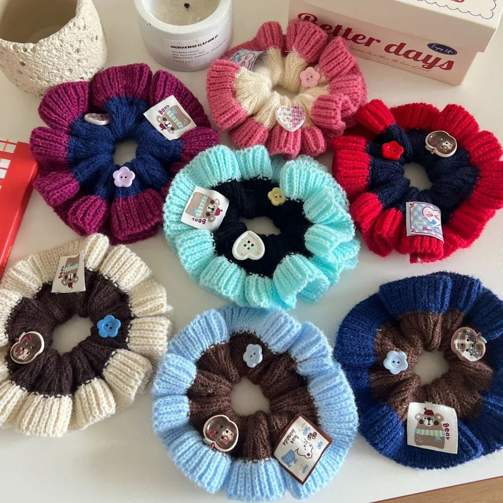 A variety of knitted flower scrunchies in different color combinations are shown from a top-down view.