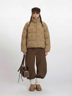 Woman wearing a tan corduroy puffer jacket with a repeating dog print, brown wide-leg pants, and a brown cap.