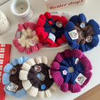 Several knitted flower scrunchies with decorative buttons and tags are displayed on a table.