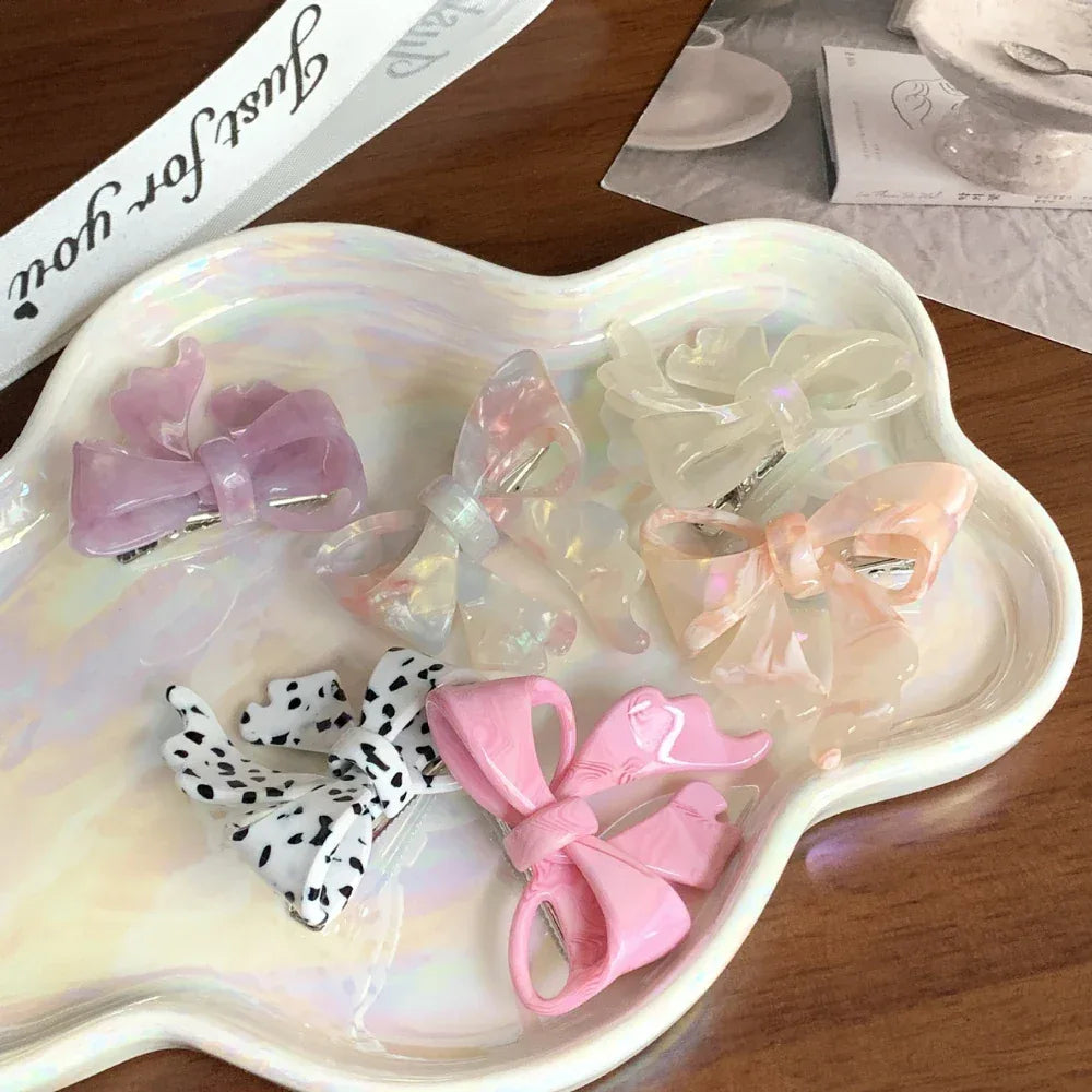 A selection of translucent and patterned bow hair clips laid out on a pearlescent tray.