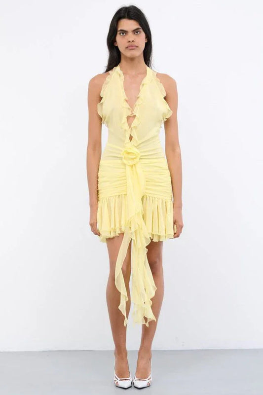 A woman wearing a yellow ruffled halter mini dress with ruching and a flower accent