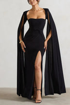 Woman wearing a floor-length black gown with a sweetheart neckline, cape sleeves, and a high leg slit.
