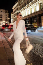 Model walking on a city street at night wearing a white draped dress.