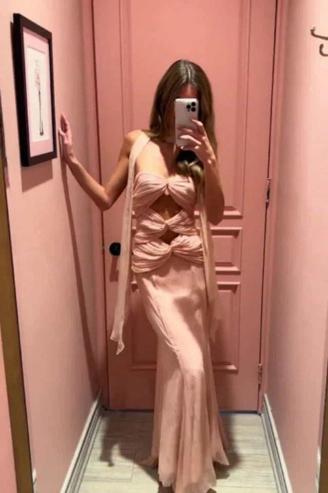 Woman taking a mirror selfie in a pale pink halter neck maxi dress with cut-out details and a mermaid hemline.