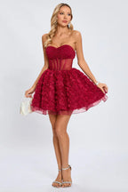 Woman holding a small white clutch and wearing a strapless red floral applique dress with sheer hem detail.