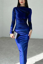 Woman wearing a royal blue long-sleeved velvet bodycon midi dress with ruching detail, holding a silver clutch and wearing silver heels.