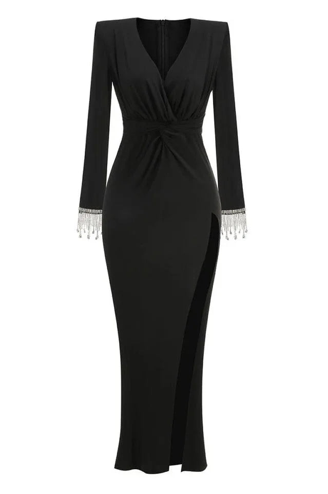 Full-length studio shot of a long-sleeved black jersey knit gown with a plunging V-neckline, ruched bodice, thigh-high slit, and embellished cuffs.