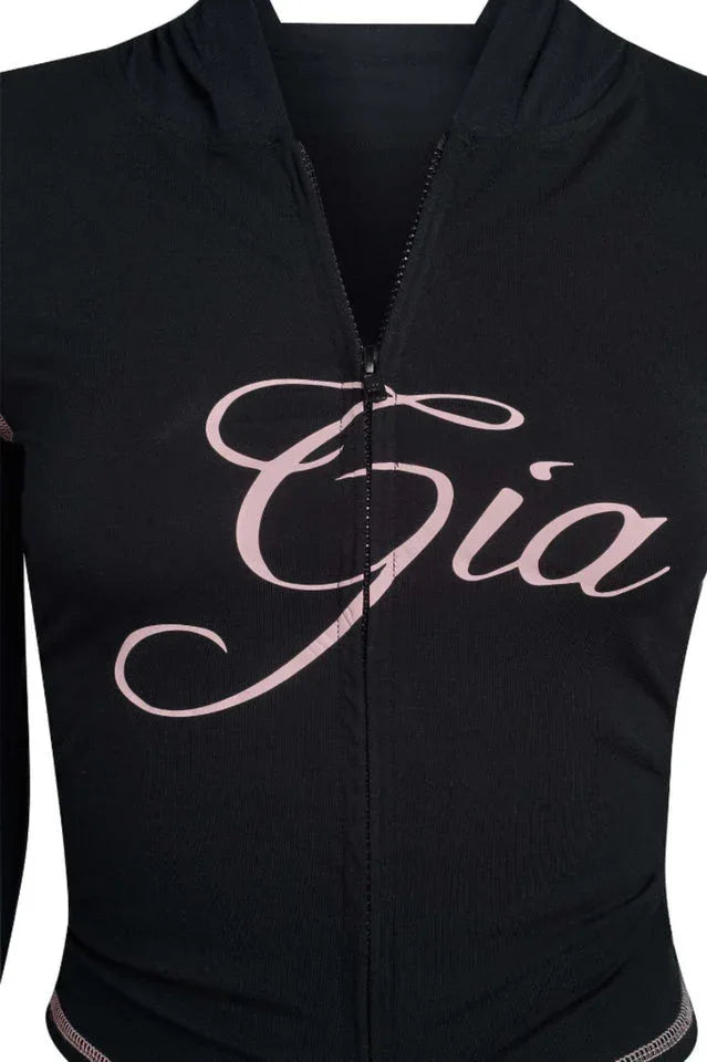 Close-up of the pink embroidered 'Gia' logo on the black zip-up top.