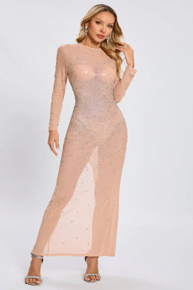 Woman modeling a long, sheer, long-sleeved gown with all-over rhinestone embellishments and a high slit. Main image