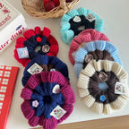 A collection of colorful knitted flower scrunchies arranged on a white surface.