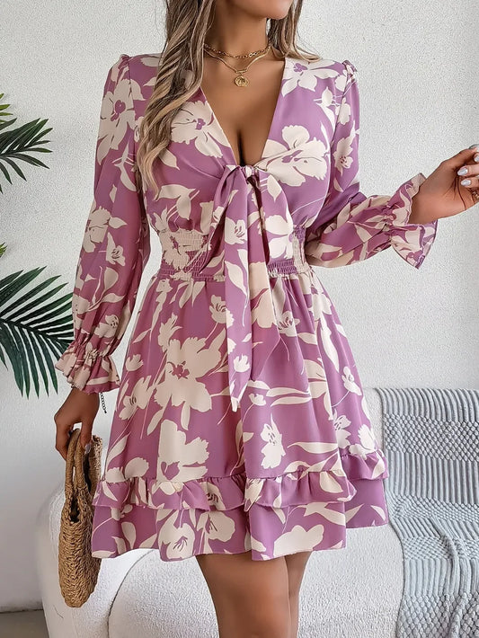 woman wearing a purple floral print mini dress with bishop sleeves and a tie front