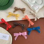 A collection of colorful resin bow-shaped hair clips arranged on a brown surface with a white textured cloth.