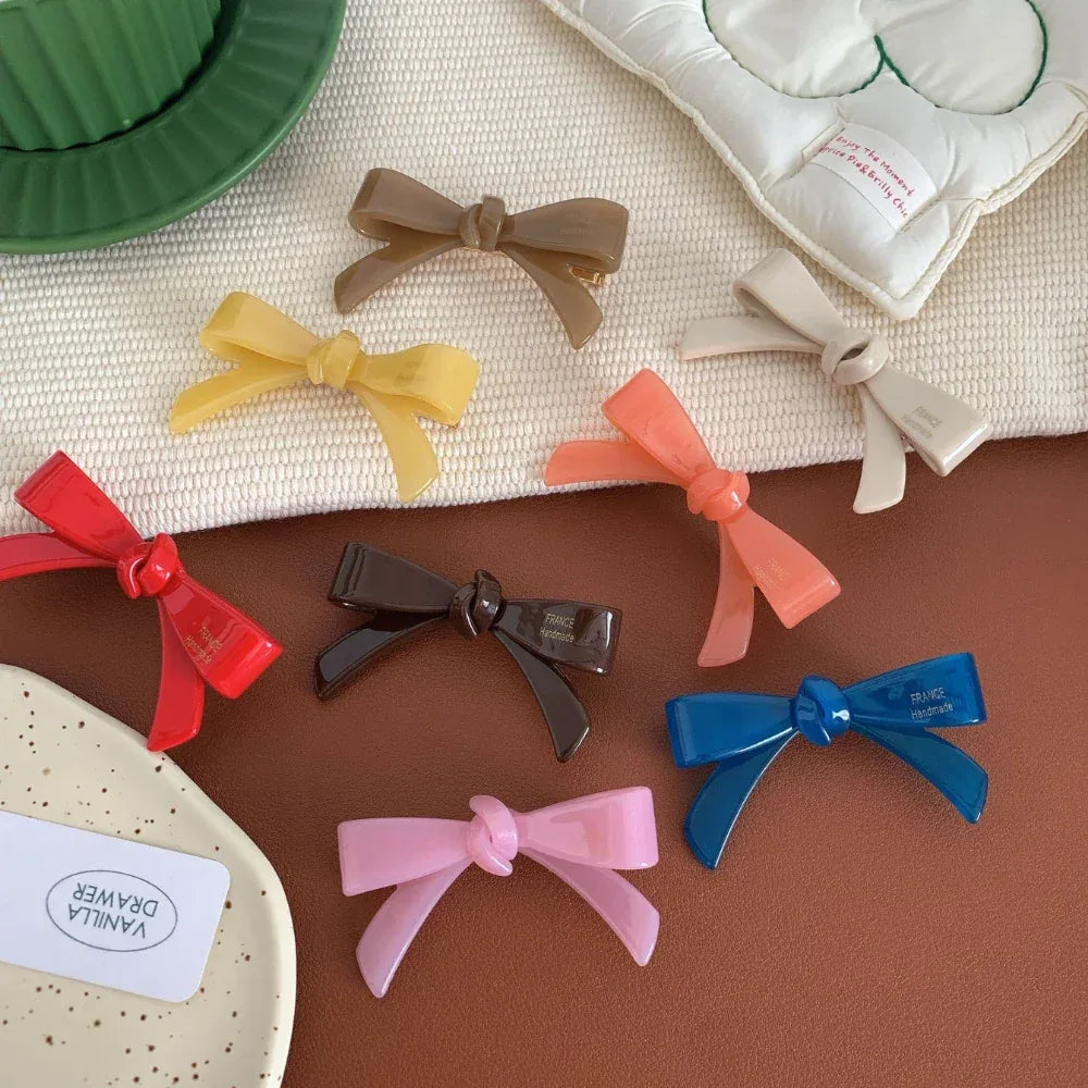 A collection of colorful resin bow-shaped hair clips arranged on a brown surface with a white textured cloth.