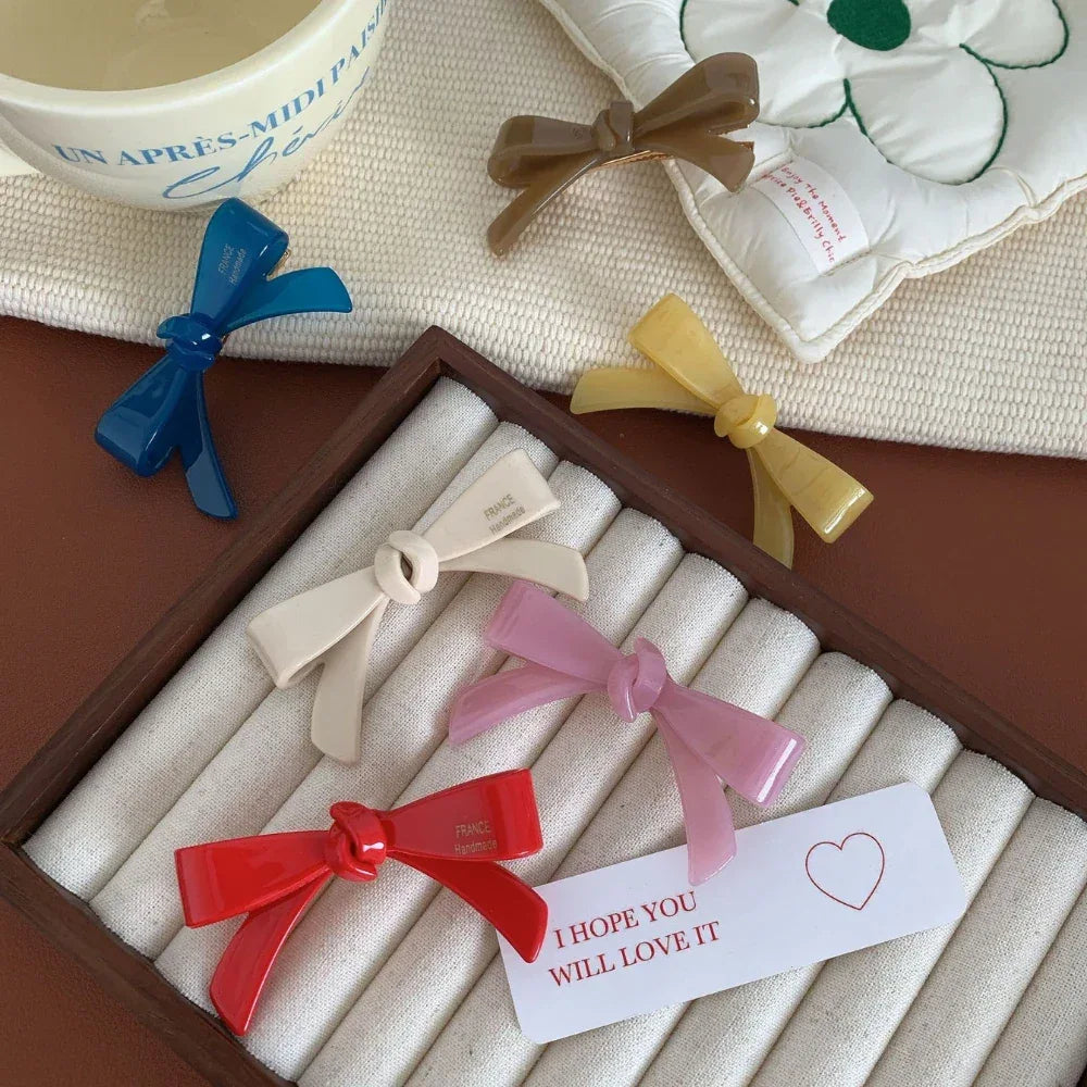 A selection of colorful resin bow-shaped hair clips displayed in a jewelry organizer with a decorative tag.