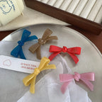 A collection of colorful resin bow-shaped hair clips laid out on a silver tray with a decorative tag.