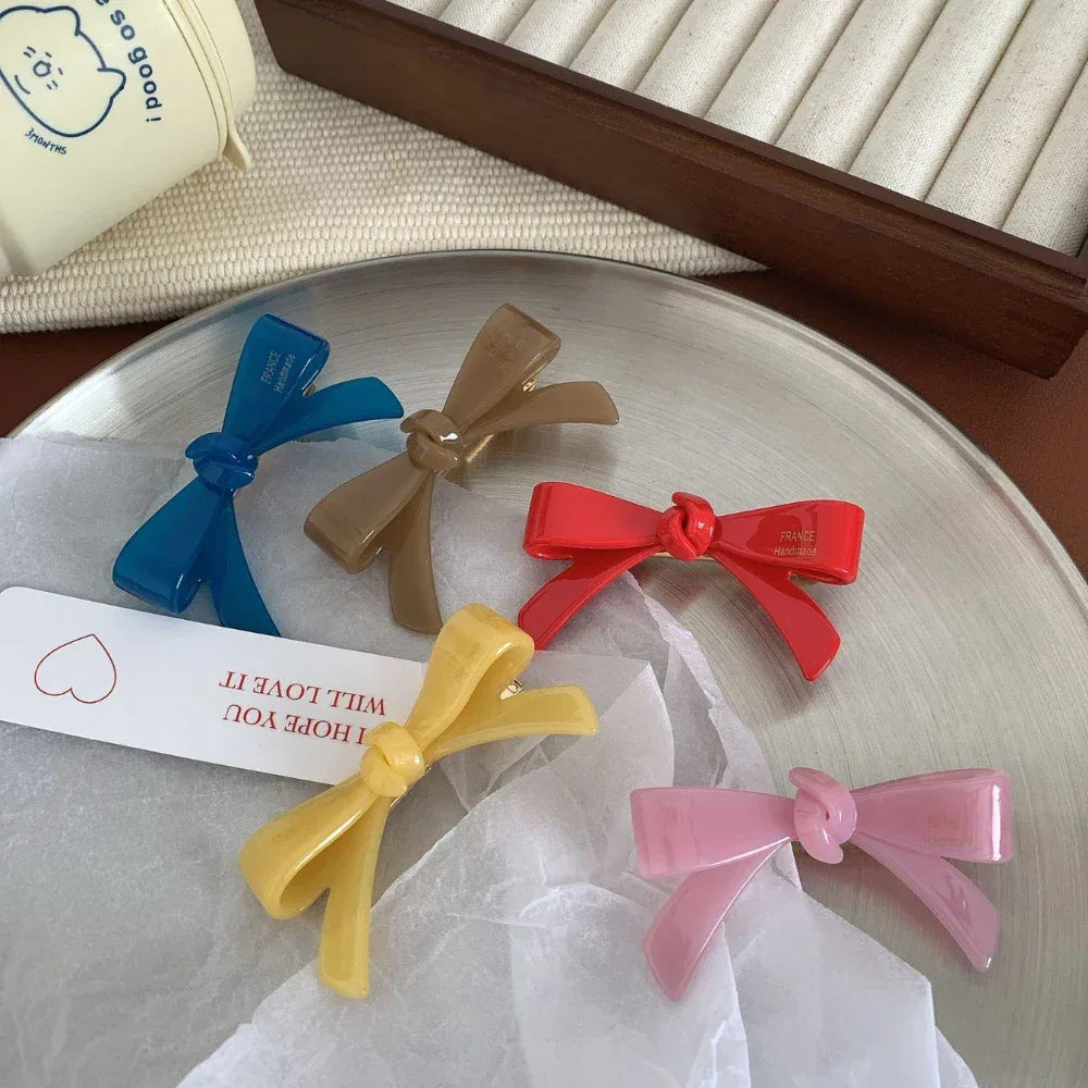 A collection of colorful resin bow-shaped hair clips laid out on a silver tray with a decorative tag.