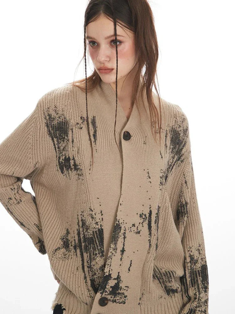 Close-up of the neckline and button closure of a distressed knit cardigan with a graphic print.