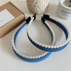 Pair of blue denim headbands with pearl trim on a white surface
