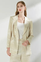 Woman with gold earrings wearing a cream jacquard suit.