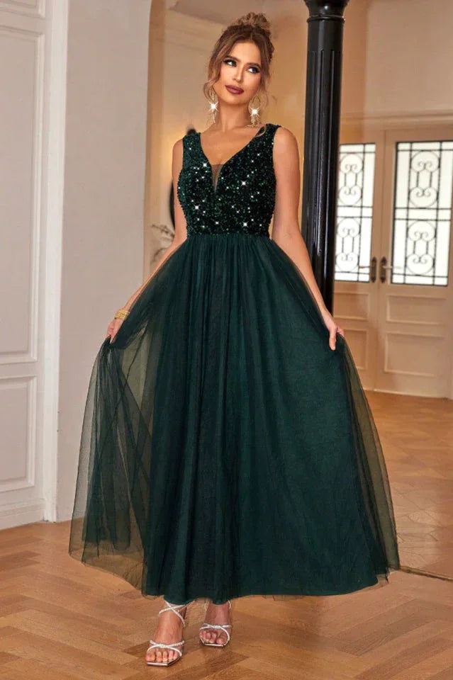 Woman in a floor-length dark green sequined and tulle formal dress with a v-neckline, holding the skirt out.