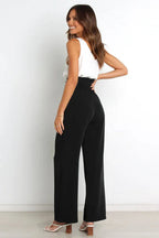 Back view of a woman wearing high-waisted wide-leg black pants with a white tank top.