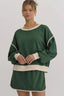 Woman wearing a green crew neck sweatshirt with cream trim and matching shorts